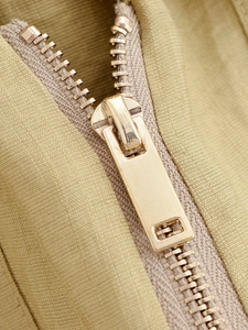 Close-up of premium light gold metal zipper on olive green textured fabric garment