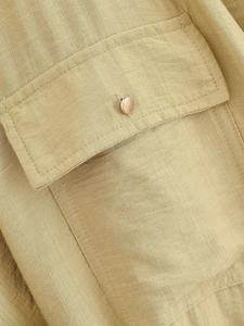 Detailed close-up of a flap pocket with rose gold button on beige linen blend fabric