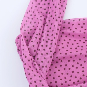 Dettaglio del tessuto a rete rosa con pois neri e trama fine a rete in primo piano