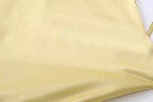 Gros plan sur le tissu satiné jaune clair montrant la texture lisse et la fine bretelle