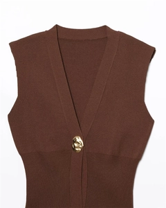 Detail of V-neck knit vest featuring a single golden irregular metal button on brown fabric