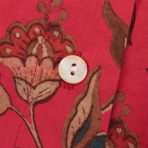 Macro detail of red floral printed fabric with a polished white button on a shirt
