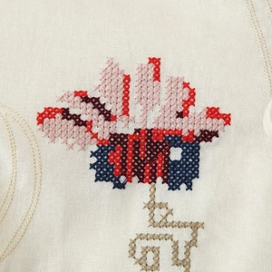 Détail de broderie de fleurs au point de croix sur une robe beige en coton et lin