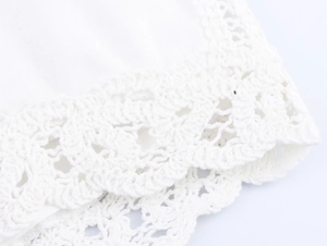 Close-up of intricate crochet lace details and hollow embroidery on ivory white fabric