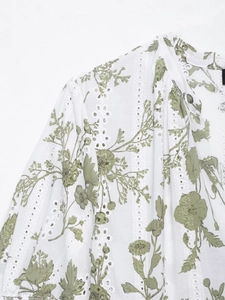 Dettaglio di un abito in cotone bianco con stampa floreale verde e ricamo traforato