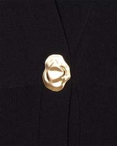 Close-up of black knit fabric texture featuring a designer gold irregular button detail