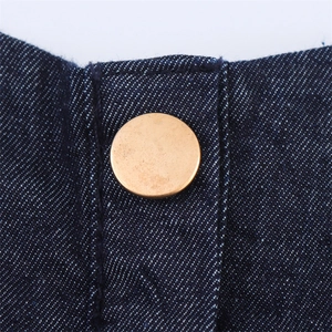 Macro detail of a vintage brass button on a dark blue denim midi dress with topstitching