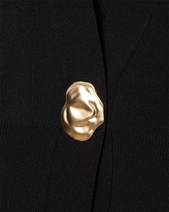 Close-up of a luxury gold lava-style metal button on black knit V-neck vest fabric