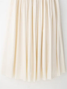 Detail view showing delicate vertical pleats of the off-white dress hem with soft fabric texture