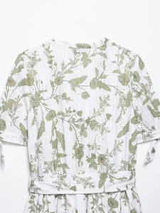 Dettaglio di un abito in cotone bianco con stampa floreale verde e ricamo traforato