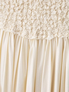 Detailed view of smocked elastic texture and pleated cream fabric on a long dress