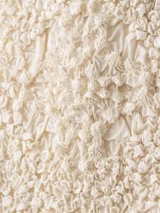 Close-up of cream textured popcorn fabric detail with 3D pleated design for long dress