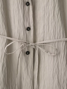 Detail von beige gestreiftem Stoff mit schwarzen Knöpfen und Taillengürtel-Bindung