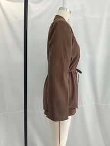 Detail view of brown belted waist jacket with buttoned cuffs and natural fabric texture