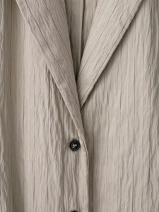 Detail eines Nadelstreifen-Blazers mit Crinkle-Struktur und glänzendem Knopfverschluss
