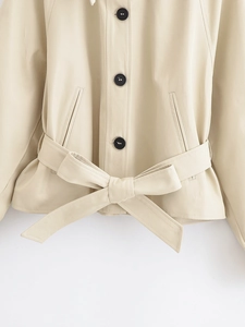 Detail of beige jacket featuring contrast black buttons and a waist belt tied in a bow