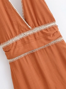 Close-up of rust-red linen dress showing deep V-neckline and white crochet embroidery