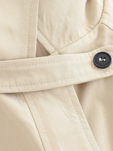 Detailed close-up of khaki trench coat fabric with matte button and belt buckle
