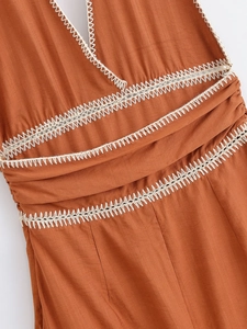 Detailed view of rust red cotton fabric with white geometric lace embroidery trim