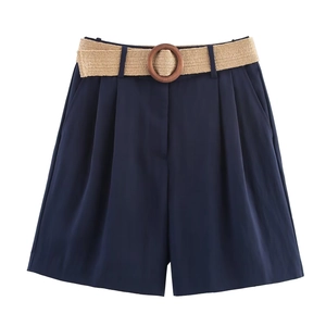 Detail of high-waisted navy shorts featuring pleats and a woven belt with wooden buckle
