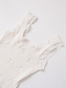 Detail eines cremefarbenen Stricktops mit feiner Spitze und kleinen Satinschleifen