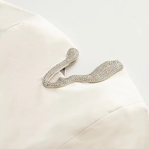 Vista macro detallada de un broche de serpiente plateado con diamantes de imitación en blazer blanco