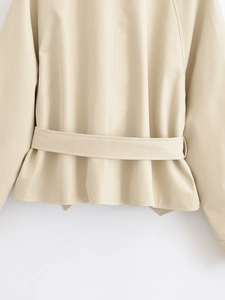 Close-up of beige trench coat back detail with adjustable waist belt and fine fabric texture