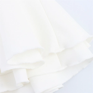 Detailed close-up of the raw fringe hemline on white fabric of the halter neck dress