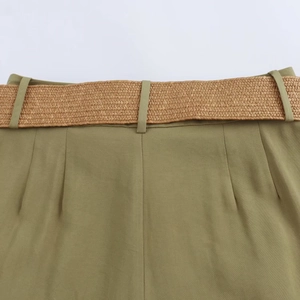 Detail of olive green bermuda shorts with pleated waist and woven straw style belt