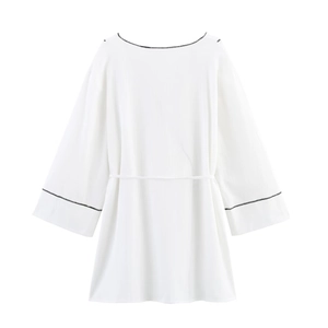 Haut blanc à manches longues avec surpiqûres noires contrastées et ceinture fine sur fond blanc