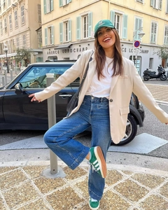 Outdoor street style view of a beige blazer paired with blue jeans and green sneakers