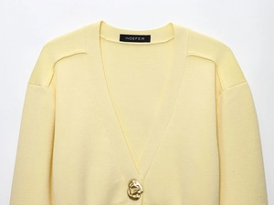 Detail of light yellow knit cardigan featuring V-neckline and irregular gold matte button