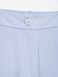 Detail of waist design with matching button and fine stitching on light blue trousers