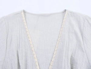 Close-up of V-neckline with delicate beige lace trim on a light gray linen-blend shirt