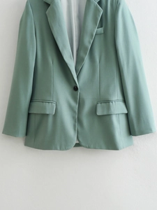 Detail of mint green blazer showing notched lapel and single button closure craftsmanship