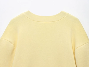 Detail of ribbed crew neck and drop shoulder seam on pale yellow knit cardigan top