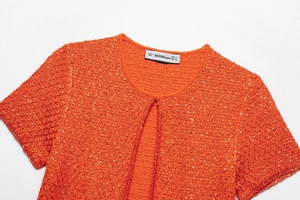 Close-up of bright orange sequined knit top showing neckline detail and brand label
