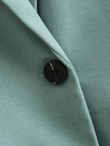 Macro shot of mint green twill fabric blazer showing a black button and sewing detail