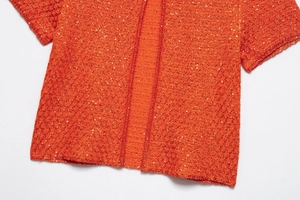 Detailed macro view of orange-red knit cardigan with shiny sequins and high-end texture
