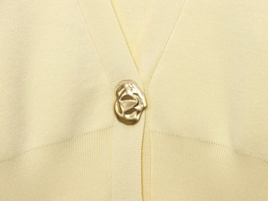Macro shot of cream knit fabric featuring a unique gold irregular metal button detail