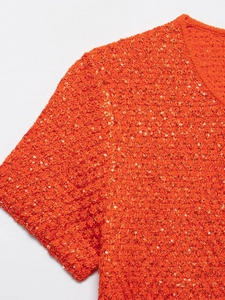 Close-up of orange knit top showing intricate gold sequins and tweed texture details