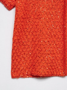 Detailed close-up of orange sequin knit fabric showing hollow crochet craftsmanship