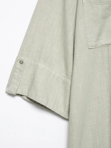 Detail of sage green linen dress showing adjustable sleeve tabs and shell button texture