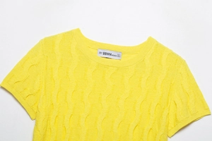 Close-up of vibrant yellow cable knit fabric with vertical wave texture and neck label