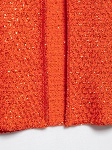 Detailed close-up of orange knit top featuring sparkling gold sequins and wavy texture