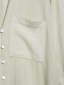 Close-up of sage green linen shirt dress featuring square pocket and pearly buttons