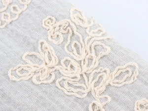 Detail of grey cotton linen fabric with intricate 3D cream embroidery and textures
