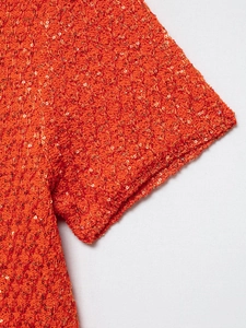 Detail of bright orange knit top featuring sparkling sequins and fine stitching