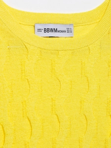 Detailed close-up of yellow knit top featuring cable pattern and white brand neck label
