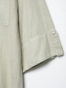 Detail of light green linen dress sleeve featuring rolled cuff and shell-texture button
